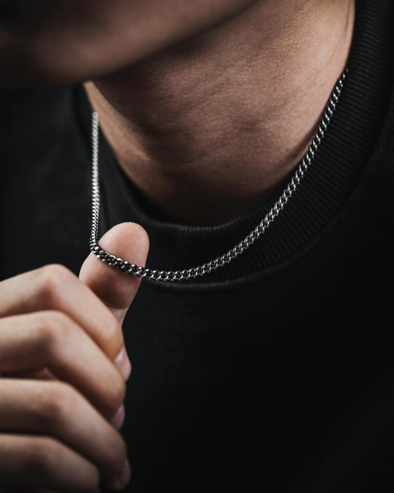 A close-up image of a person's hand touching a silver necklace, showcasing elegant jewelry.