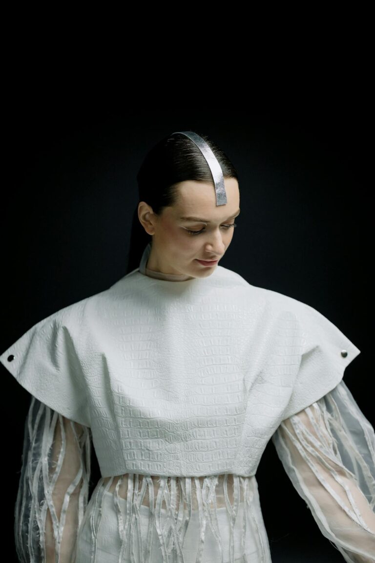 A woman in futuristic attire with metallic hair accessory, gazing downward.