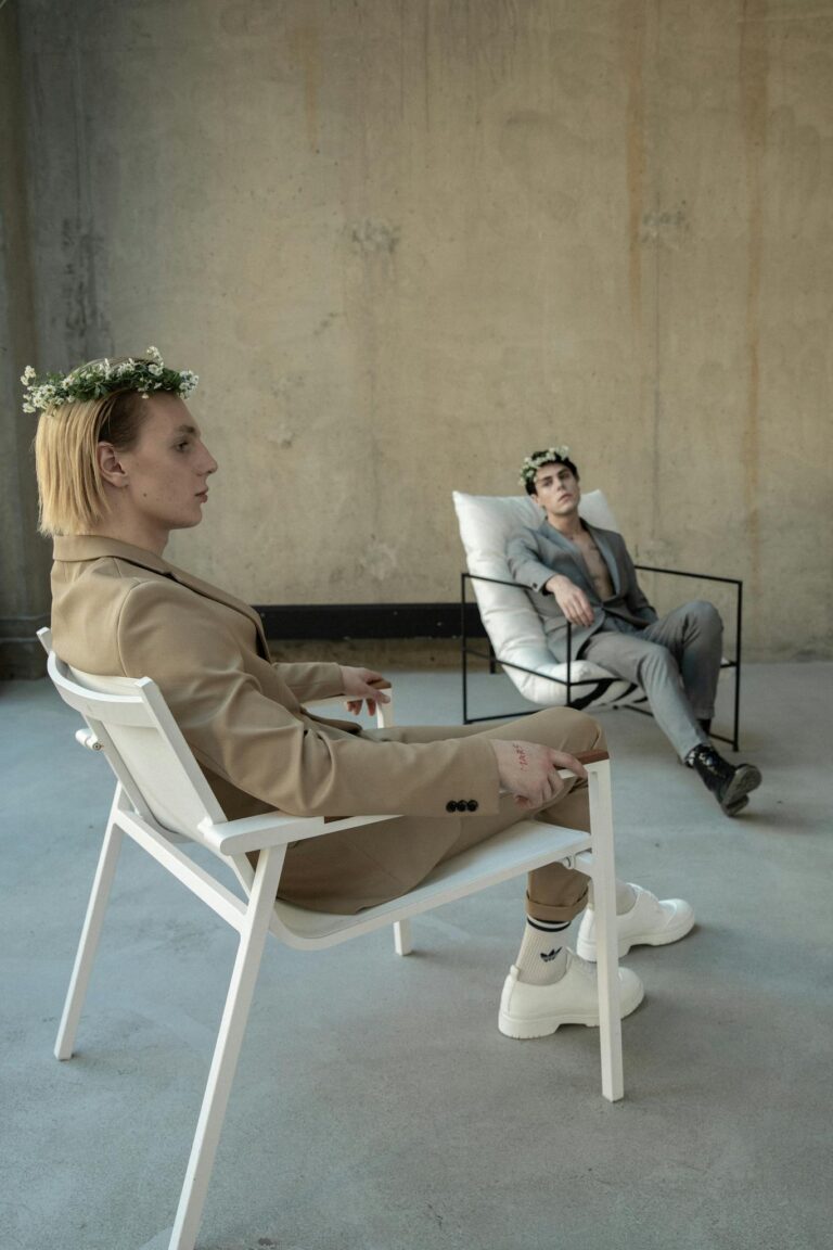 Two stylish men in suits with flower crowns indoors, highlighting modern fashion.