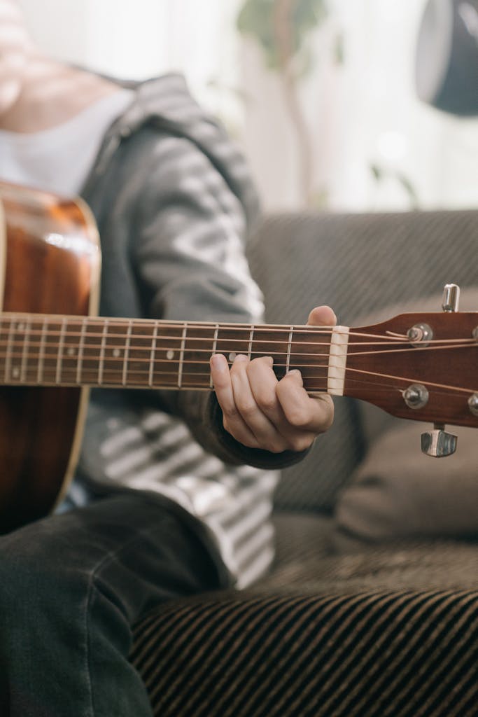 A person strums an acoustic guitar indoors, capturing a moment of musical creativity.